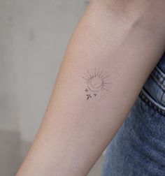 a woman's arm with a small sun and arrow tattoo on the left inner arm