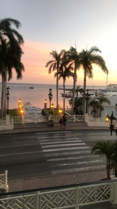 the sun is setting over the ocean with palm trees and people walking on the sidewalk