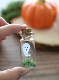 a person holding a tiny glass bottle filled with green moss and a ghost in it