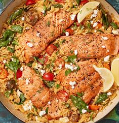 a pan filled with chicken and rice topped with tomatoes, lemon wedges and spinach