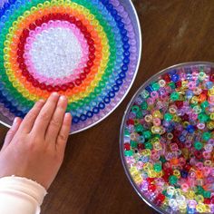 a child's hand next to a bowl of beads and a plate with a rainbow design on it