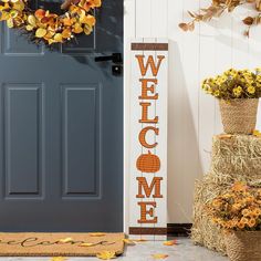 a welcome sign next to a blue door with hay and fall leaves on the ground