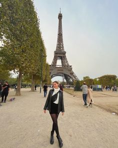 a woman standing in front of the eiffel tower with her legs crossed and black boots on