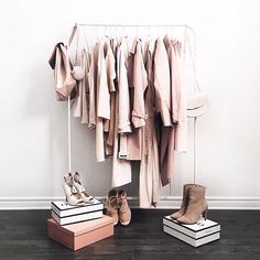 clothes and shoes are hanging on a rack in front of a white wall with wooden flooring