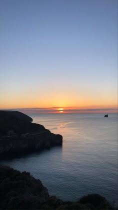 the sun is setting over the ocean and some hills in the distance with boats out on the water