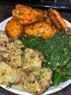 a white plate topped with potatoes and spinach covered in gravy next to chicken wings