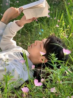 a woman laying in the grass reading a book with her eyes closed and head up