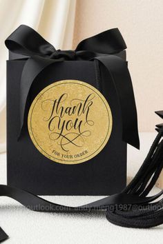 a black and gold thank you gift bag with tassels on the side next to it