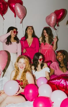 a group of women sitting on top of a bed with pink and red balloons in the air