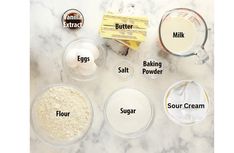 ingredients to make an egg muffin laid out on a marble counter top, including flour, sugar, butter, milk and eggs