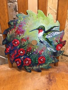 a painting of a hummingbird sitting on top of a wooden chair with red flowers