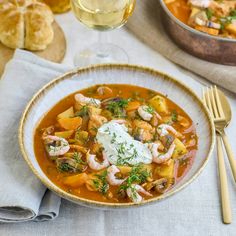 a bowl of soup with shrimp, potatoes and sour cream on the side next to a glass of wine