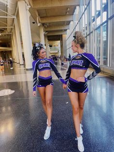 two cheerleaders are walking down the hall together in purple outfits and white sneakers