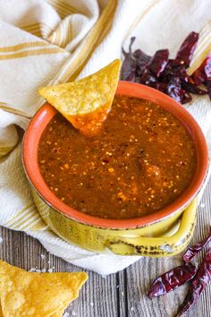 a tortilla chip being dipped into a bowl of salsa with chips on the side