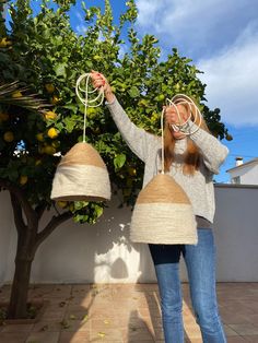 a woman is holding two lamps in front of her face while standing next to a lemon tree