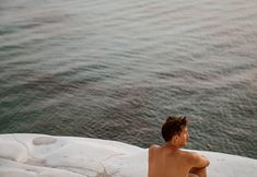 a man sitting on top of a rock next to the ocean with his back turned