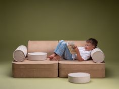 a young boy reading a book while sitting on a couch with two round ottomans