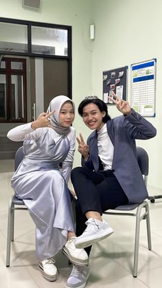 two women sitting on chairs posing for the camera with their fingers up in front of them