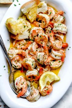 a white bowl filled with shrimp and lemons on top of a table next to bread