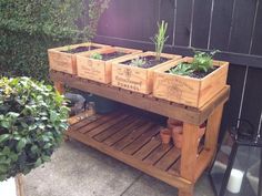 four wooden planters with plants in them sitting on a table outside next to a fence