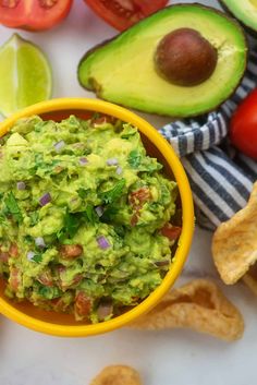 a yellow bowl filled with guacamole surrounded by tortilla chips and tomatoes