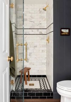 a white toilet sitting next to a walk in shower with black and white tile on the floor