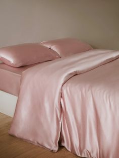 a bed with pink sheets and pillows on top of wooden flooring in front of a white wall