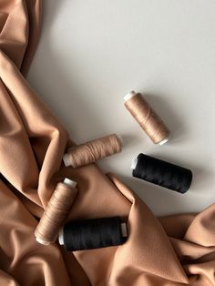 three spools of thread sitting on top of an orange satin material covered table