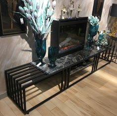 a table with vases and flowers on it in front of a wall mounted fireplace