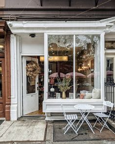 a white table and two chairs in front of a storefront with an open window