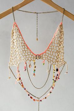 a piece of clothing hanging on a wooden hanger with beads and chains attached to it