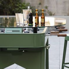 an outdoor table with bottles and glasses on it, next to two bar stools