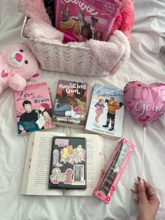 a pink teddy bear sitting on top of a bed next to some books and balloons