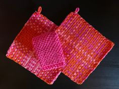 two pieces of pink and orange knitted cloth on a black table with red string