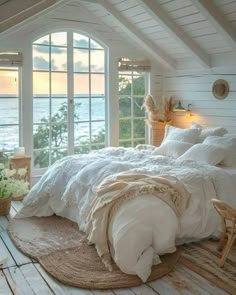 a bedroom with white walls and flooring has a large bed in the corner, along with two windows that look out onto the water