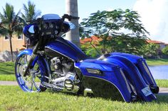 a blue motorcycle parked on top of a lush green field next to a lake and palm trees