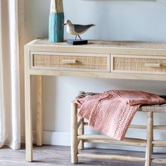 a bird is sitting on top of a wooden table next to a pink blanket and blue vase