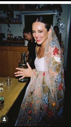 a woman wearing a veil holding a bottle in her right hand and smiling at the camera