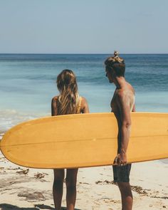 two people are standing on the beach with their surfboards and looking at the ocean