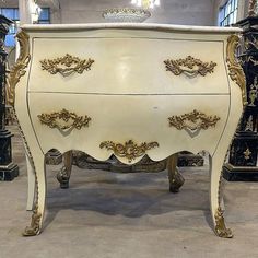 an ornate white and gold painted chest of drawers in a room with other antique furniture