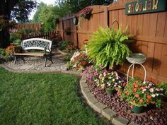 a garden area with flowers, plants and a bench in the middle of the yard