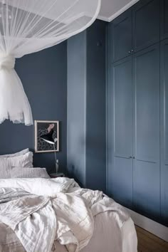 a bedroom with blue walls, white bedding and mosquito netting hanging from the ceiling