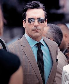 a man in a suit and sunglasses standing next to other people