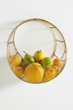 a wire basket filled with fruit on top of a white wall