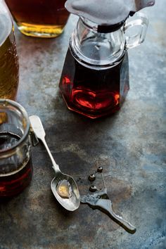 a spoon with some liquid in it next to two jars filled with honey and syrup