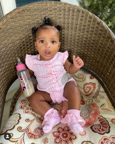 a baby sitting in a wicker chair with a bottle