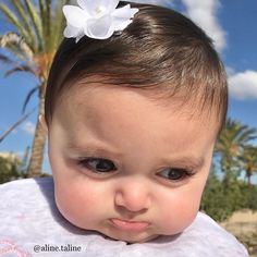 a close up of a baby with a flower on her head and palm trees in the background