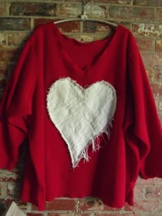 a red sweater with a white heart on the front and back, hanging against a brick wall