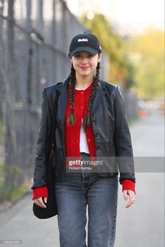 a woman walking down the street wearing a black hat and leather jacket with braids