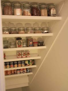 an open pantry door with jars and spices on the bottom shelf in front of stairs